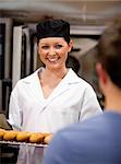 Smiling female baker holding baguettes ready to serve her customer in a bakery