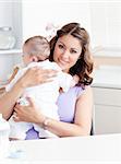 Positive young mother holding her baby in the kitchen at home