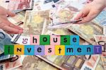 toy letters that spell house investment with cash in hands against a money background with clipping path