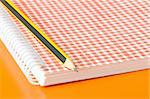 pencil and notebook over an orange background