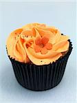 A freshly baked cup cake with orange frosting