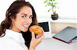 Happy hispanic businesswoman eating a doughnut in her office