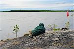 The tourist has a rest on rocky coast of evening lake