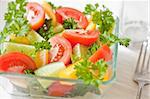 Fresh vegetables: tomatoes, cucumbers, a paprika and parsley in a plate. Near the fork and transparent glass