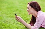 Delighted young woman on phone sitting on the grass in a park