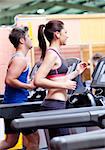 Pretty woman with earphones using a treadmill with her boyfriend in a fitness centre