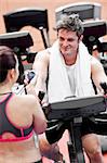 Happy athletic man on a bicycle looking at his coach in a fitness centre