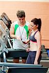 Happy woman listening to her coach after doing exercises on a treadmill in a sport centre