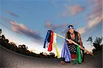 Indigenous man squatting in the middle of a road with ceremonial pole and flags in the middle of a road with ceremonial pole representing seven directions