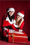 two woman in Santa costume opening christmas gift. on red