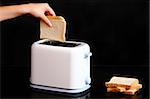A picture of a female hand putting a piece of toast to a toaster over black background