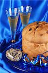 Panettone the italian Christmas fruit cake served on a blue glass plate over a yellow background and two glasses of spumante (sparkling wine). Selective focus.