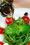 Close up macro photograph of olive oil dressing being poured onto a fresh rocket and basil salad with cherry tomatoes and balsamic vinegar