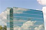 Sky and clouds are reflected in the mirrored windows of this modern office building.