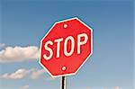 A red octagonal stop sign with blue sky and clouds in the background.