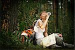 beautiful young woman sitting under tree in forest with backpack and map, drinking water with her eyes closed
