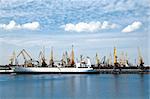 big cargo ship at big sea port with lots of cranes, blue cloudy sky in background