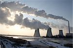 View of coal power plant against sun with several chimneys and huge fumes
