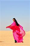 Beautiful young woman  in pink eastern dress dancing in arabic desert