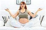 Pregnant woman sitting in meditating  on sofa at home.