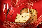 Panettone the italian Christmas fruit cake served on a red glass plate over a red background with golden star decorations, ribbon and two glasses of champagne. Selective focus.