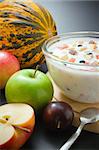 Glass bowl filled with yogurt mixed with fruit pieces arranged with spoon and some fruits around