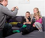 Father taking a photo of his family siting in the sofa