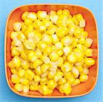 Bowl of canned corn on a vibrant blue background.