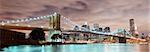 New York City Manhattan panorama view with Brooklyn Bridge at night with office building skyscrapers skyline illuminated over Hudson Rive