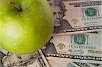 A green apple sits on top of a pile of $20 bills to illustrate the cost of education, food, or health care.