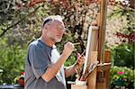 Man paints on an easel in a pleasant outdoor setting.