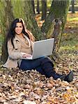 Beautiful woman working on laptop in park during autumn season