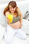 Smiling beautiful pregnant woman sitting on sofa at home with glass of juice  in hand. Close-up.