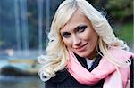 close up fashion portrait of a blond girl with hair style in black coat and pink scarf with forest in background