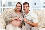 Happy couple showing an echography to the camera both sitting on the sofa at home