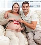 Lovely couple putting baby shoes on the woman's belly sitting in the living room