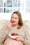Hungry pregnant woman eating strawberries sitting in the living-room at home