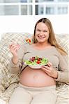 Cheerful pregnant woman eating vegetables in the living room