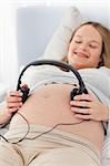 Happy pregnant woman putting headphones on her belly lying on a bed