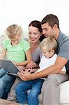 Parents and children using their laptop together sitting on the sofa at home