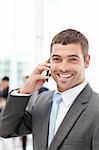 Happy hispanic businessman on the phone while his team is working in the background