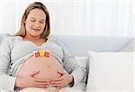 Pretty pregnant woman with letters on her belly resting on a bed