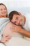 Happy man listening the belly of his pregnant wife both on the bed