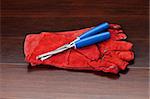 Red gloves and blue chisels on dark wooden floor