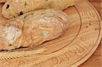 Olive bread on a carved beech wood board with wheat.