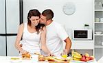 Affectionate man kissing his girlfriend while cutting bread for breakfast in the kitchen