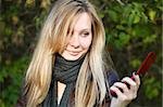 Young cute girl with long blond hairs with cell phone. Fall. Autumn. Outdoor session.