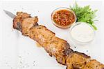 Grilled pork kebab with sauce and greens on white plate