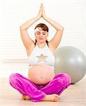 Beautiful pregnant woman doing yoga on floor at living room