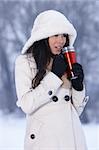 Beautiful woman holding thermal mug in snowy winter outdoors